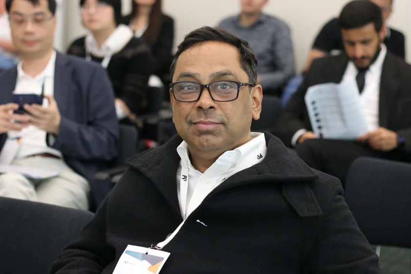 A conference participant with a name badge, seated in the audience